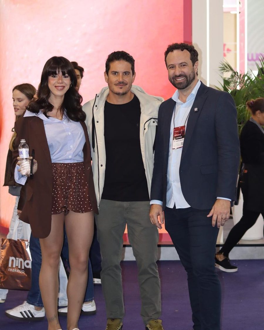 Reunião de três pessoas à mesa em estande de feira cosmética